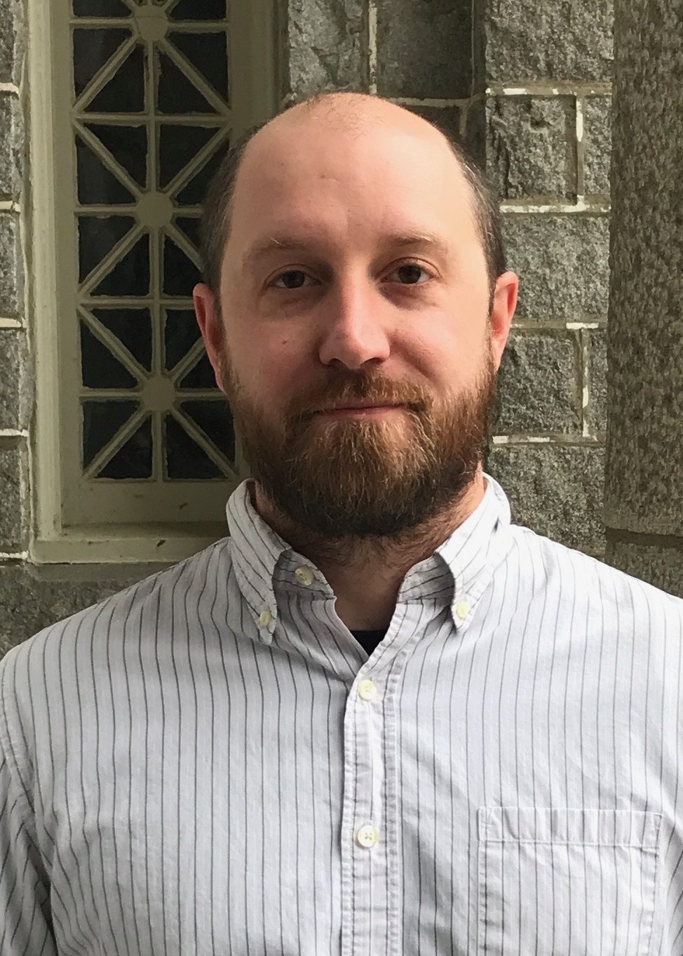 Headshot of Dr. Benjamin Guenther. He is wearing a striped button-up shirt.